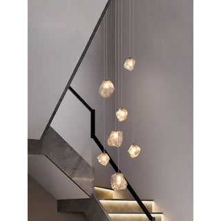 Rock glass pendant chandelier suspended along a modern black-railed staircase with warm LED glow
