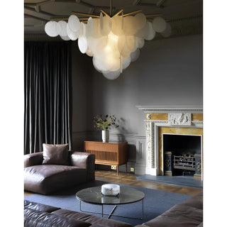 Sculptural glass disc chandelier glowing warmly in a moody luxury room with fireplace and velvet curtains