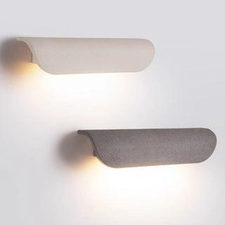White and gray microcement wall lights with warm LED glow, front view