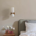 Minimalist double wall sconce with glossy white glass and brass finish installed above a bedside table