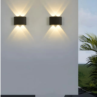 Outdoor installation of two minimalist black LED wall lights mounted side by side, illuminating a white exterior wall