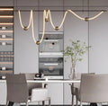 MIRODEMI irregular linear LED pendant light with silicone wave design and brass accents, illuminating a minimalist gray kitchen with dining table