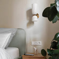 Modern brushed brass wall sconce with glossy white glass shades installed beside a contemporary bed