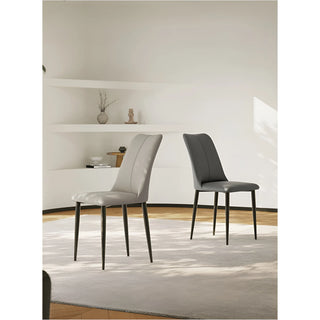 Two modern dining chairs with curved backs and faux leather upholstery in a minimalist living space.
