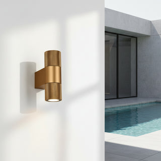 Modern gold industrial wall light mounted outdoors beside a minimalist poolside wall, casting a soft glow