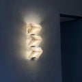 Three-light marble wall sconce glowing at night with soft wall wash effect