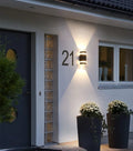 Matte black LED wall light installed next to a wooden entrance door, casting warm glow