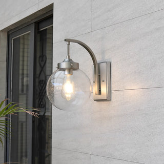 Modern waterproof outdoor wall light with stainless steel arm and clear glass globe, mounted on exterior wall near patio door