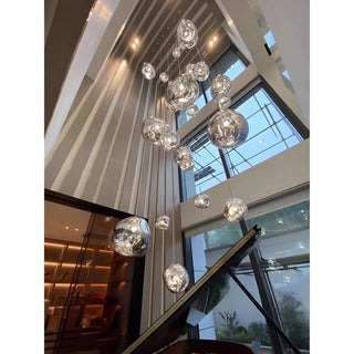 Modern multi light glass staircase chandelier installed in a tall luxury interior with architectural lines and large windows