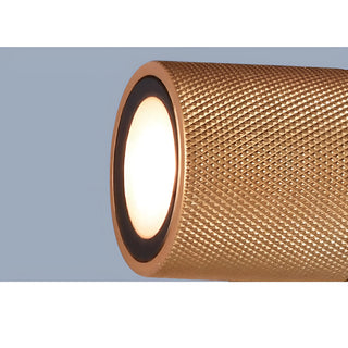 Zoomed-in image of a gold textured cylinder from a modern LED wall sconce, emitting warm light with a black ring frame