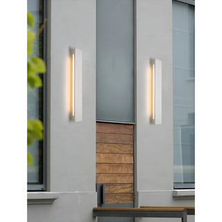 Modern vertical white outdoor wall sconce mounted on a gray building facade near wood paneling