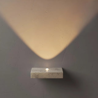 minimalist travertine stone wall lamp casting an upward warm light on a textured wall