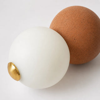 Close-up of the Orbara pendant's frosted glass orb and brick-red micro-cement bead with a brass ring