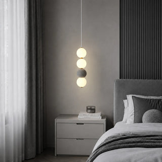 Gray Orbara stacked-sphere pendant beside a bed and nightstand in a minimalist gray bedroom