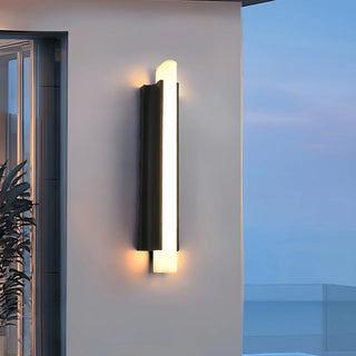 Modern outdoor wall sconce glowing warmly in the evening on exterior house wall
