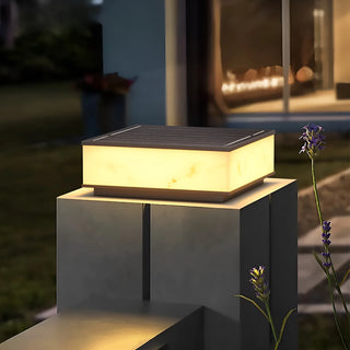 Close-up view of a waterproof marble-finish solar pillar light with soft warm LED glow in a garden setting