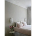 Two handcrafted textured glass wall sconces installed symmetrically beside a modern bed with blush pillows and soft neutral decor