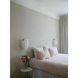 Two handcrafted textured glass wall sconces installed symmetrically beside a modern bed with blush pillows and soft neutral decor