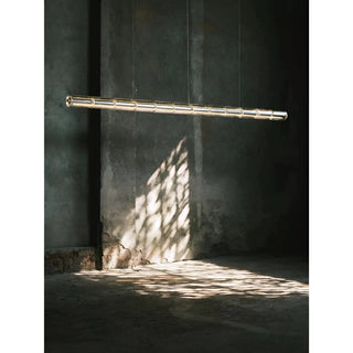 Glass tube pendant light hanging in a raw industrial loft with textured concrete walls and dramatic shadows on the floor