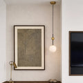Sleek pendant light with white glass shade hanging in the corner of a minimalist bedroom
