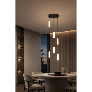 Warm-lit Pluvara capsule chandelier over a round dining table at dusk with floor-to-ceiling windows