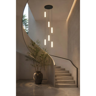 Pluvara capsule pendant lighting a curved entry staircase with a potted tree in a warm modern home
