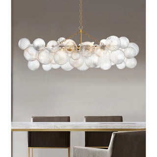 Rectangular clear glass chandelier with gold frame hanging above a dining table in a bright dining room.