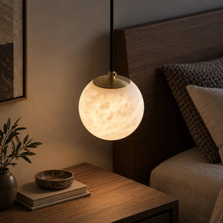 Selenara alabaster globe pendant light with a brass canopy glowing beside a bed