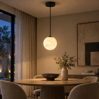Selenara alabaster globe pendant with a black canopy above a round dining table at dusk