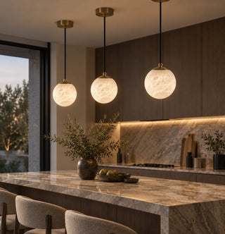 Three Selenara alabaster globe pendants with brass canopies over a marble kitchen island