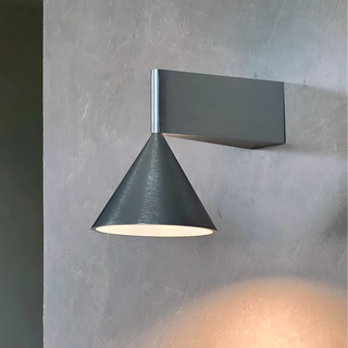 Brushed silver Bauhaus wall sconce with cone shade casting elegant light on textured wall