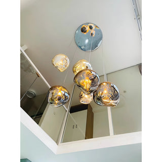 Elegant smoky gray glass chandelier installed above a staircase, creating a floating bubble lighting effect