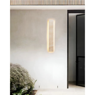 Handcrafted travertine wall sconce glowing warmly on a serene, minimalist patio entrance