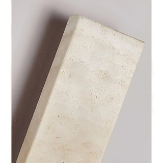 Side-angle view of Solea wall sconce highlighting smooth honed travertine surface in natural light