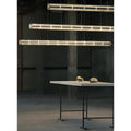 Three linear pendant lights installed at different heights in an industrial-style room above a minimalist white table