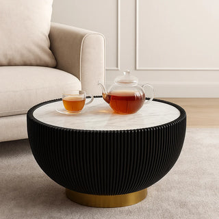 Black round coffee table with marble top and gold base decorated with glass teapot and cups