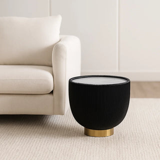 Black round side table with gold base and marble top next to beige sofa in modern interior
