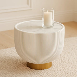 White round side table with gold base and marble top featuring a lit candle on beige carpet