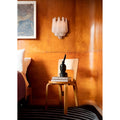 Sculptural Murano-inspired glass wall light displayed against rich wood paneling beside a minimalist chair and side table