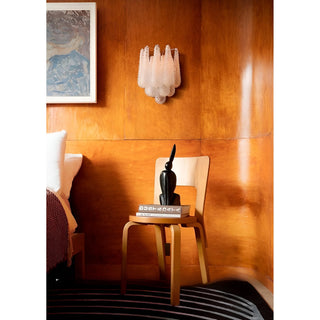 Sculptural Murano-inspired glass wall light displayed against rich wood paneling beside a minimalist chair and side table
