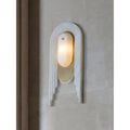 Modern marble and brass wall sconce mounted on a textured beige wall, glowing with warm light