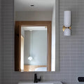 Brushed brass wall sconce with glossy white glass shades mounted beside a bathroom mirror